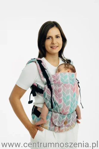 Mama nosząca niemowlę w ergonomicznym nosidle klamrowym w pastelowy wzór liści.
